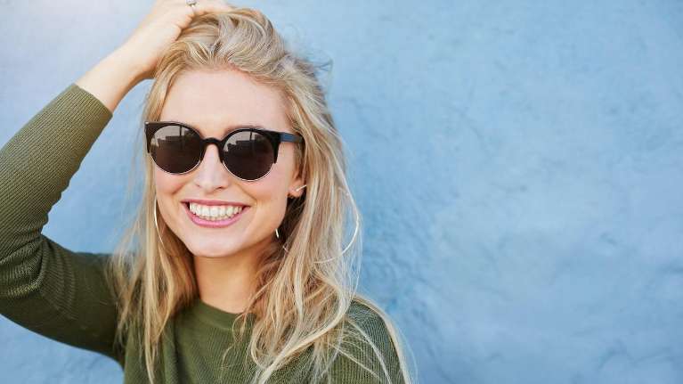 woman in sunglasses highlights her bright smile, representing the top choice for teeth whitening
