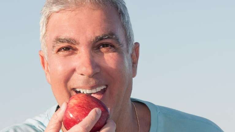 A man bites a crisp apple, showing healthy teeth and good nutrition.